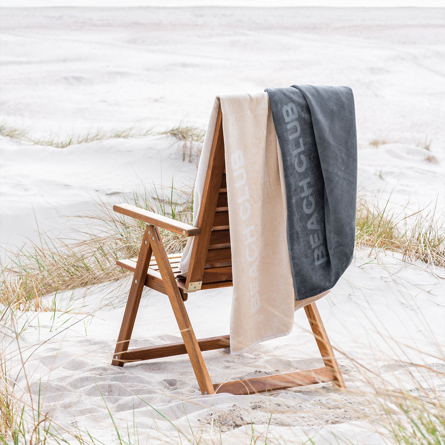 Zwei beige und graue Strandtücher auf Holzliegestuhl in den Dünen am Strand